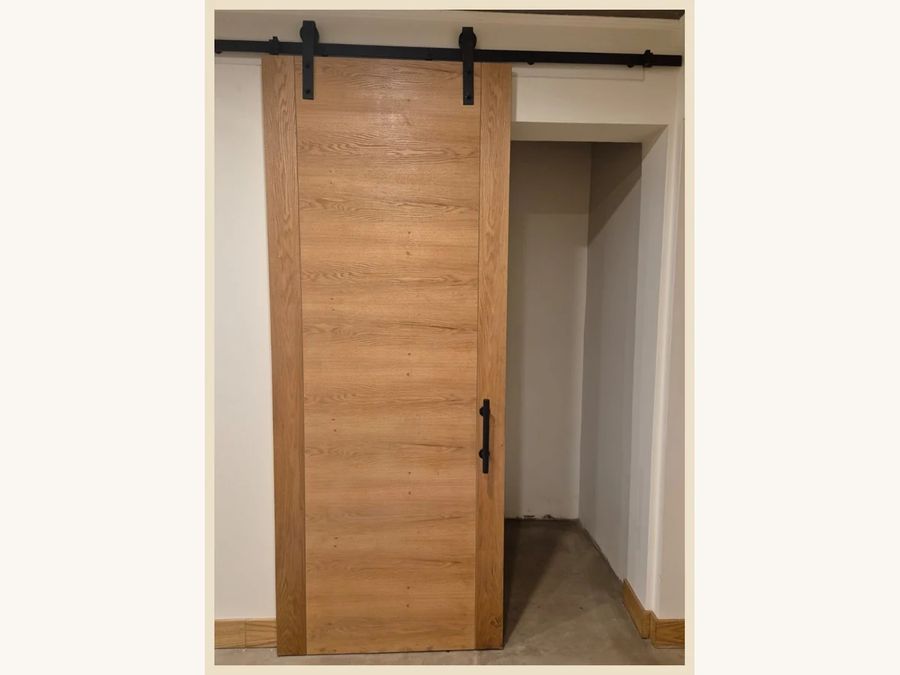 Puerta corredera con riel a la vista modelo Capri con 2 canterías verticales, MDF enchapada en Encina Blanca